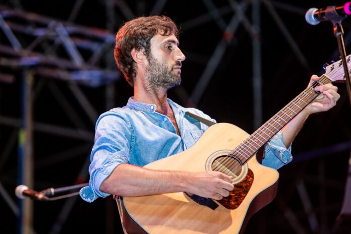 nella mia pelle - vincenzo capua in primo piano, durante un concerto, indossa camicia azzurra e ha la chitarra acustica a tracolla