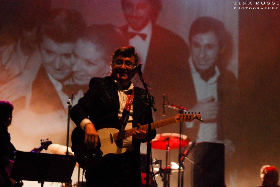 bobby solo in concerto, indossa un vestito scuro e ha la chitarra elettrica a tracolla