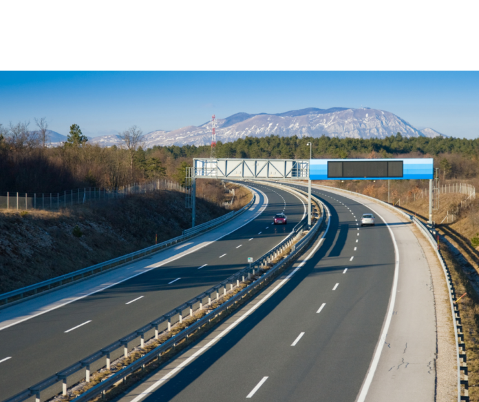 Autostrade per l'Italia - un'autostrada vista dall'alto con sullo sfondo un traliccio per l'elettricità e una montagna