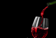 etichettatura del vino - nella foto su sfondo nero brilla un bel calice di vno rosso e si vede il collo della bottiglia da cui è versato
