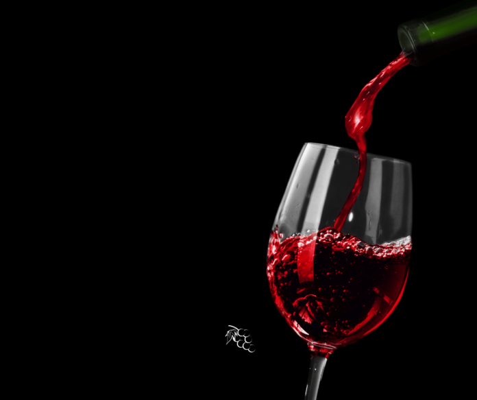 etichettatura del vino - nella foto su sfondo nero brilla un bel calice di vno rosso e si vede il collo della bottiglia da cui è versato