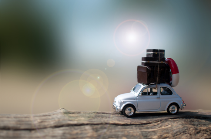 viaggi e vacanze - nella foto una vecchia cinquecento fiat bianca con delle valige sul tetto sta rullando sulla sabbia con il sole