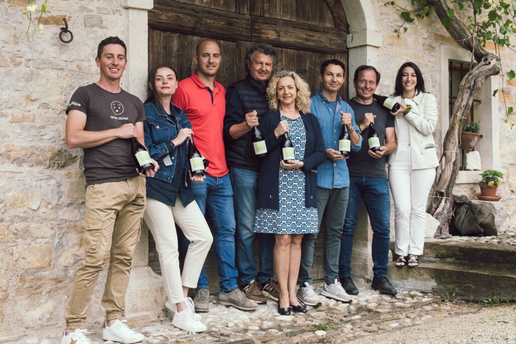 viticoltura - una foto della famiglia Biasi davanti alla loro azienda agricola. Ognuno di loro ha in mano una bottiglia di vino