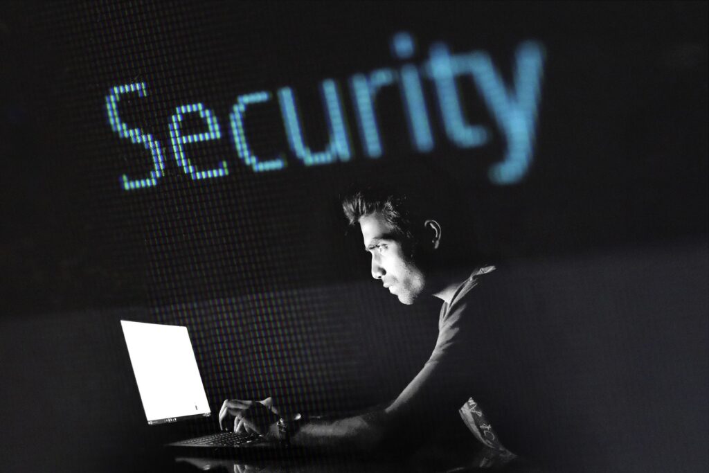 truffe digitali - nella foto tutta nera illuminata solo dalla luce dello schermo di un pc un uomo sta digitando sulla tastiera. In alto la scritta blu "security"