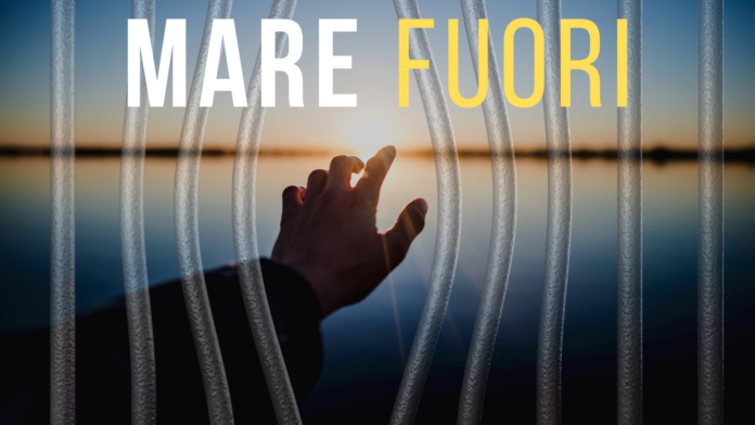 Mare fuori, napoli, camorra, mare fuori, stagione, netflix, mare, carcere, ipm, carcere minorile. Una braccio allungato con sfondo il mare al tramonto dietro le sbarre. In alto la scritta MARE FUORI