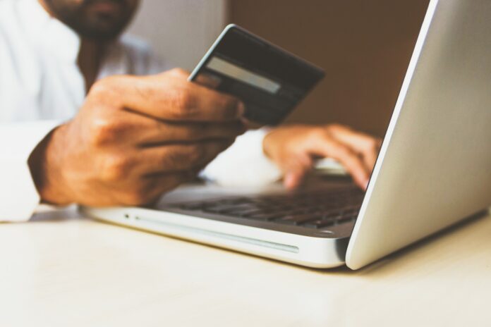 pagamenti digitali - un uomo tiene in mano una carta di credito mentre digita qualcosa sulla tastiera di un pc portatile grigio
