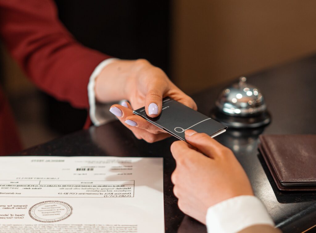 Pagamenti a rate - la mano di un areceptionist dell'hotel di cui si vede la manica della giacca color granata, sta dando la chiave ad un cliente . Si vedono sul tavolo il modulo di prenotazione e il campanellino di chiamata della reception