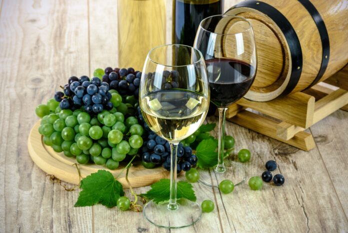 viticoltura - due bicchieri di vino, uno bianco e uno rosso, dietro un tagliere di legno con dell'uva rossa e bianca e una piccola botte di legno