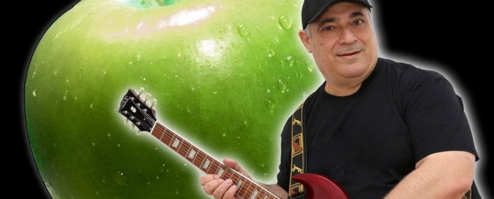 il tempo delle mele - gibo che indossa cappellino e maglia neri, imbraccia una chitarra elettrica, sullo sfondo una mela verde
