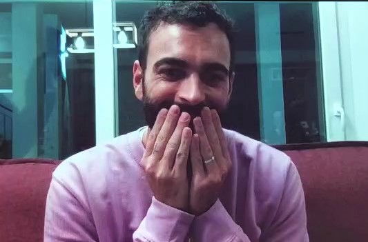 marco mengoni indossa una felpa rosa e ha le mani appoggiate alle guance