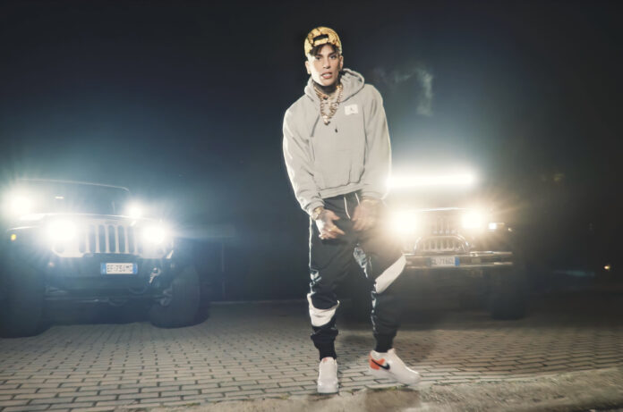 mc drive - il rapper rayan seventeen17 indossa una felpa beige e pantaloni di una tuta di colore bianconero. è illuminato dai fari di due jeep