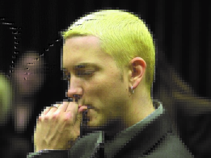Eminem di profilo, con capelli cortissimi gialli, ha la mano sotto il mento ed ha l'aria pensierosa
