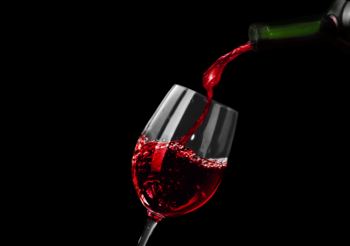 Vinitaly - sfondo nero, un bicchiere leggermente piegato dove si sta versando del vino dal colore rosso brillante