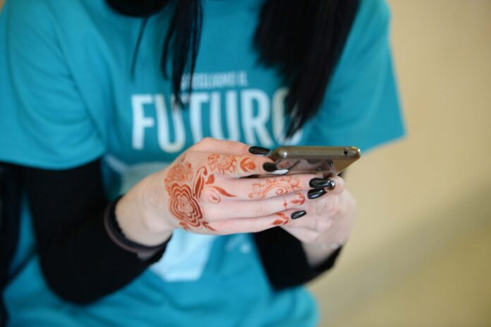 una donna tiene in mano n cellulare con magletta blu con scritto futuro