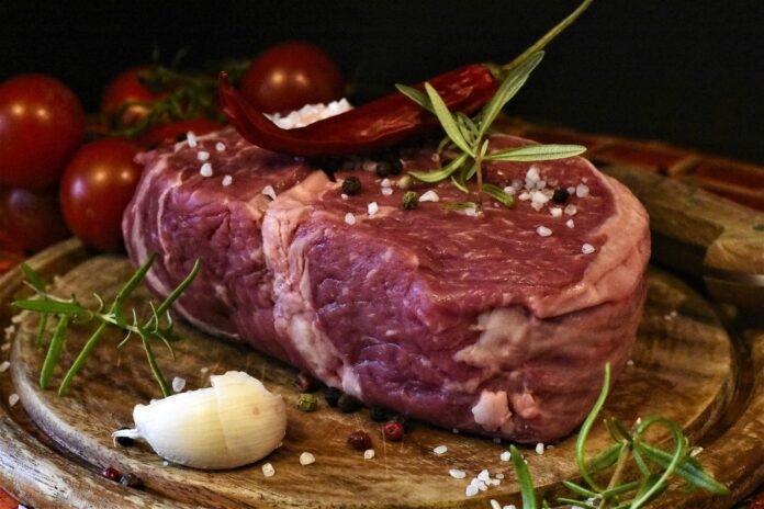 carne sintetica - una bistecca rossa bella spessa, appoggiata su un tagliere di legno, condita con spezie