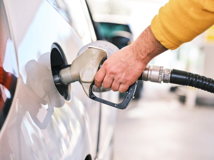 biocarburanti e rinnovabili - il primo piano di una mano con manica gialla che sta mettendo carburante nel serbatoio dell'auto con una pompa di benzina
