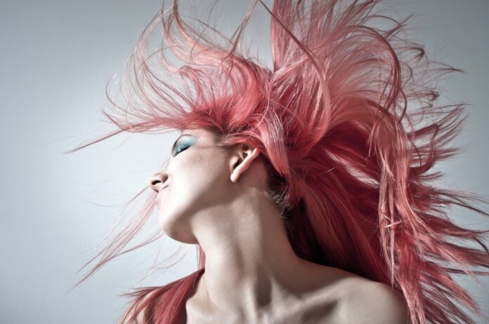 cantautrici rappresentate nella foto dal primo piano di una donna con i capelli rosa meentre gira la testa facendoli agitare al vento