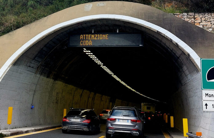 PRIMO MAGGIO 2023 - UNA CODA DI AUTO IN AUTOSTRADA STA IMBOCCANDO UNA GALLERIA SULLA CUI SOMMITà C'è UN CARTELLO CHE DICE 