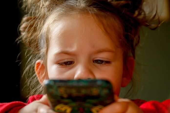 minorenni internet - primo piano di un abimba che ha gli occhi incrociati mentre guarda il cellulare