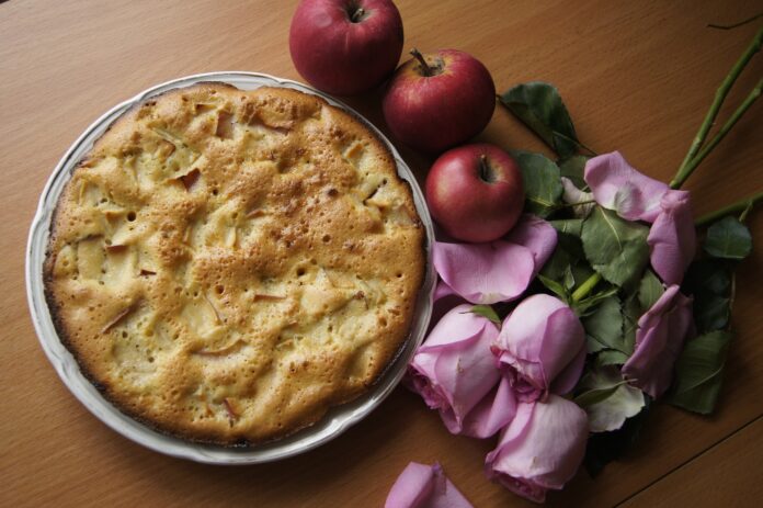 fiori in cucina - una torta rotonda e affianco delle rose rosa e delle mele rosse