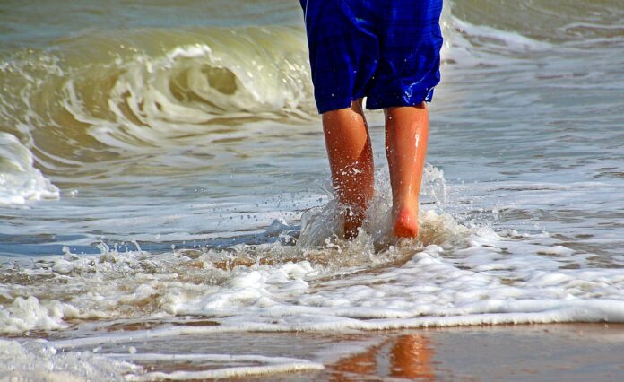 mattia rame - primo piano delle gambe di un uomo, con i boxer azzurri, che cammina sul bagnasciuga