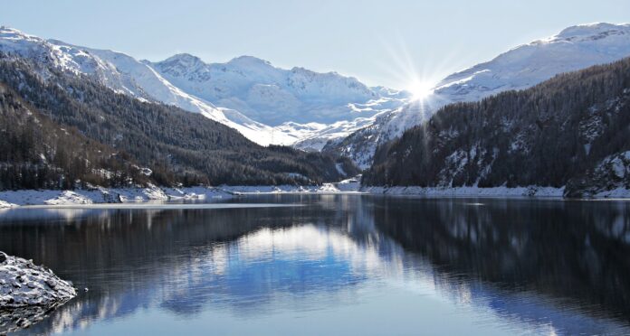 neve del futuro - un bellissimo panorama di montagna con le cime innevate, ils ole che spunta dietro le vette e in primo piano, un lago bellissimo in cui si riflettono le montagne