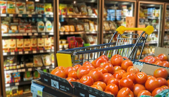 prezzi - un supermercato di cui si vedono i frighi e in primo piano un carrello della spesa e delle cassette di pomodori
