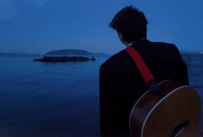 gabriele esposito di spalle, con a tracolla una chitarra acustica. sullo sfondo il mare