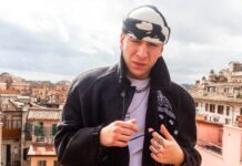 fasma in primo piano. Indossa t shirt bianca, giaccone scuro e in testa porta un berretto bianconero