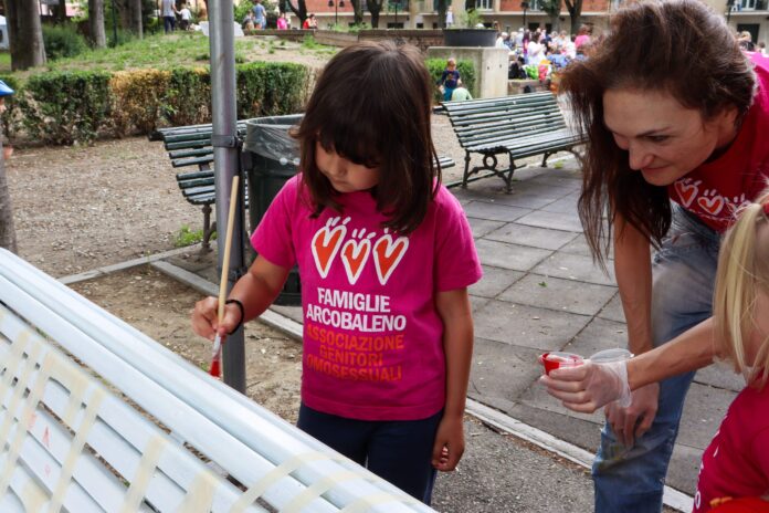 un momento di allestimento della panchina delle famiglie promossa da torino e rosso indelbile una donna e una bambina con maglie rosa con scritta famiglia è chi famiglia fa pitturano con clori arcobaleno una panchina