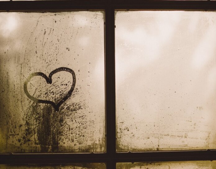 un cuore disegnato col dito su un vetro di una finestra da cui si vede che piove