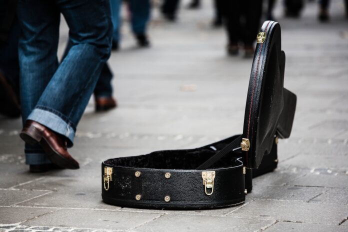 la custodia di una chitarra aperta appoggiata su un marciapiede e le gambe di alcuni passanti