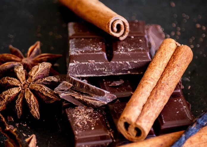 cioccolato a tavolette spezzato con dei cilindri di cialda e dei fiori di cacao in una composizione artistica