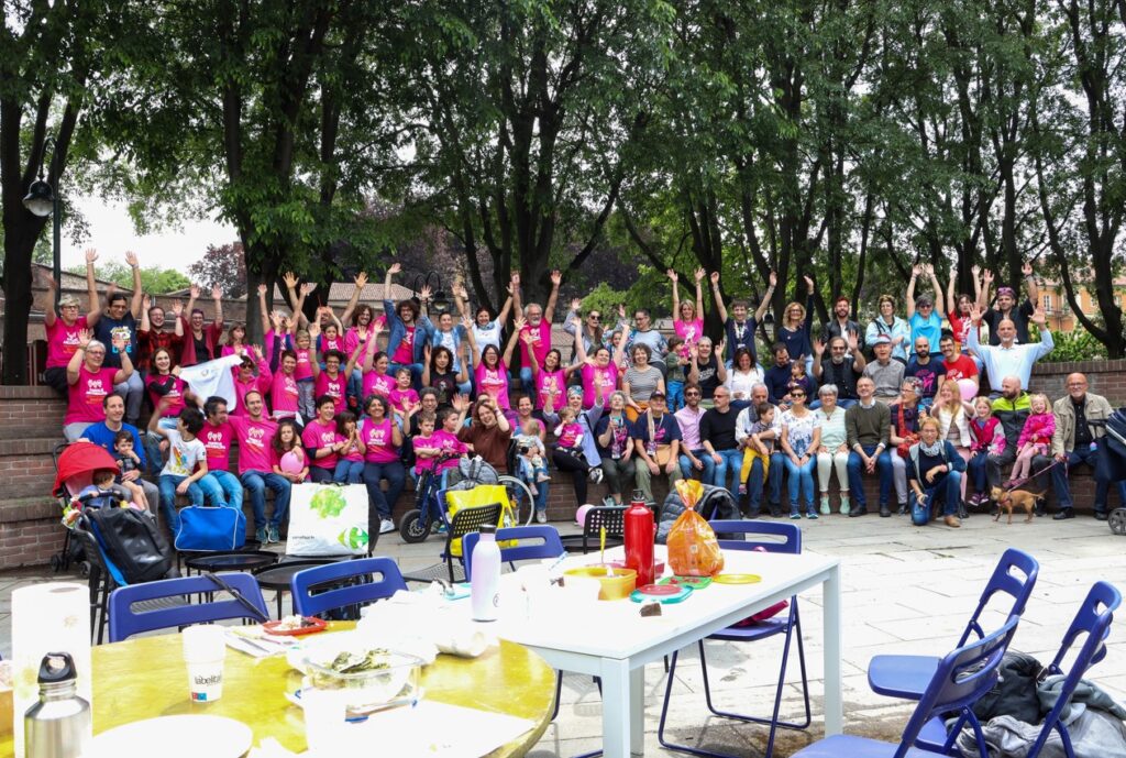 foto di gruppo con adulti e ragazzi introno alla panchina delle famiglie con maglia rosa con scritta nel giardino