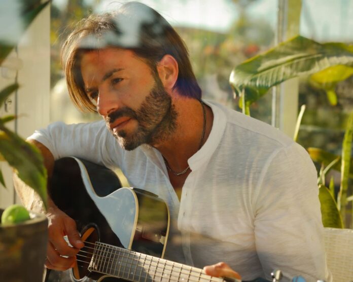 fabio martorana in primo piano, indossa una camicia bianca e imbraccia una chitarra di legno nero