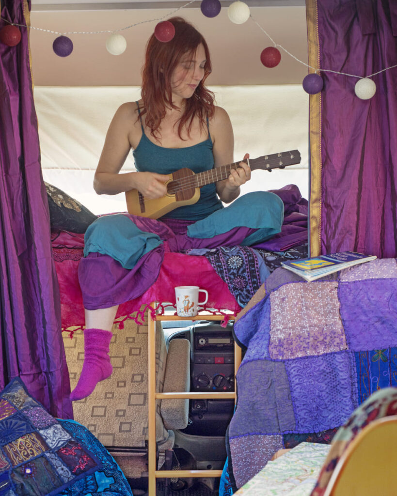 nathalie all'interno di un camper, è vestita con abiti colorati e ha in mano un ukulele