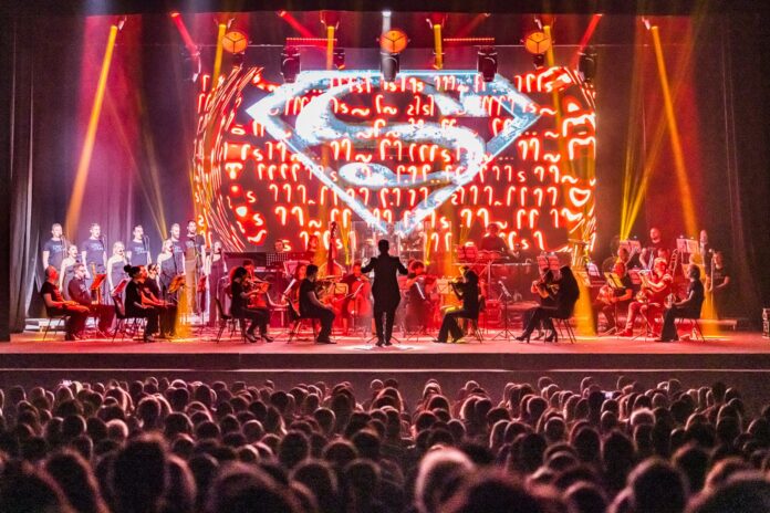 hans zimmer - l'orchestra lords of the sound sul palco durante un concerto. sullo sfondo il logo di superman
