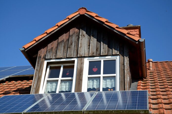 Pannelli fotovoltaici transizione energetica - un pannello solare sul tetto di una casa che ha una èpiccola finestrella di legno con un cuoricino sul vetro