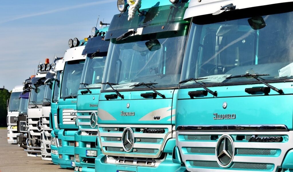 veicoli elettrici - tanti Tir parcheggiati in fila, quattro azzurri e gli altri bianchi, con il simbolo della mercedes