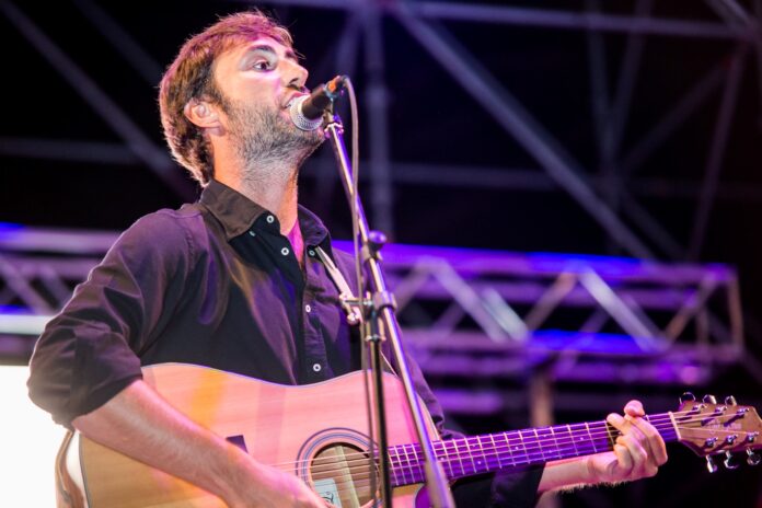 bella - vincenzo capua dal vivo, indossa una camicia scura e ha una chitarra acustica a tracolla