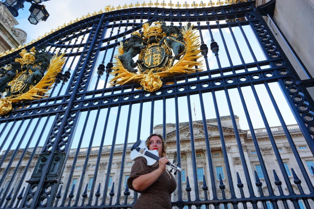 beatrice limonti, vestita di scuro, con un violino bianco in spalla, fotografata davanti al caancello di buckingham palace a londra