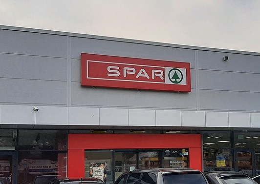 DESPAR il logo un triangolo verde dentro un cerchio verde e sotto su sfondo rosso la scritta DE in grigio e SPAR in bianco