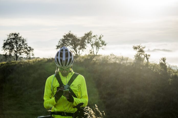 il cellulare non prende, in mano a un ciclista fermo tra le montagne, Il ciclista indossa una felpa gialla fosforescente e un caschetto