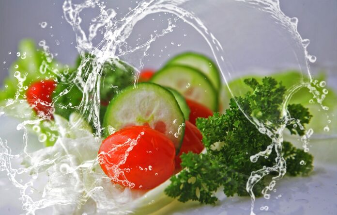 green food - nella foto insalata, pomodori e fettine di cetrioli annaffiati da un getto d'acqua