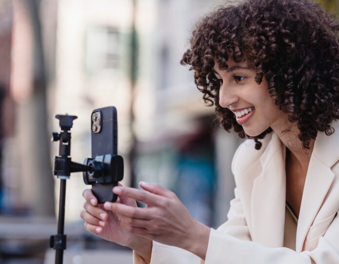 influencer con capelli lunghi e ricci sorride davanti a cellulare