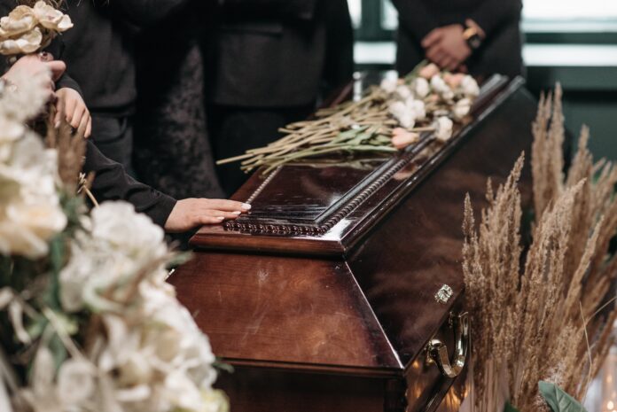 bara pompe funebri - nella foto il primo piano di un abara circondata da fiori e delle mani appoggiate sopra