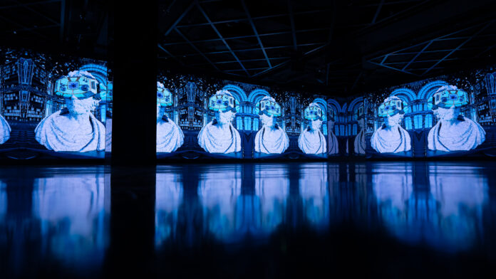 arte digitale - una mostra in un asala completamente buia illuminata dai quadri che riflettono una luce azzurra e nei quali si vede la sagonma di un uomo che indossa degli occhiali per realtà virtuale
