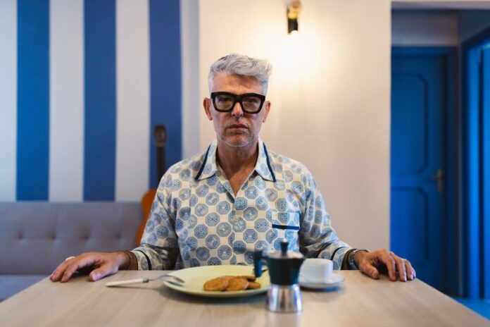 dr myine, davanti a un tavolo apparecchiato per la colazione, indossa occhiali da vista con la montatura nera e un pigiama bianco a disegni azzurri