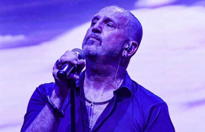 gianni salamone, durante un concerto, indossa una camicia blu, e ha l'asta del miscorofono nella mano destra