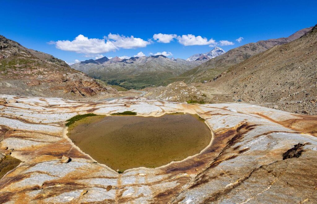 quel che resta del ghiacciaio dei  forni: tra due montagne un avalle qausi snza neve con dell'acqual al centro